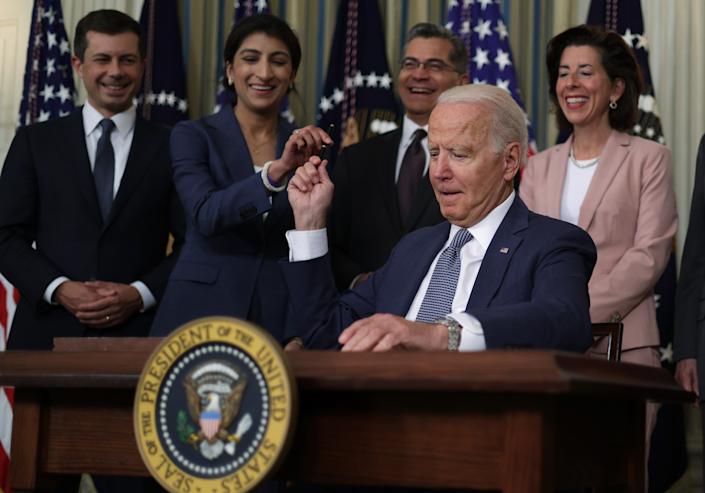 WASHINGTON, DC - JULY 09:  U.S. President Joe Biden passes a signing pen to Chairperson of the Federal Trade Commission Lina Khan (2nd L) as (L-R) Secretary of Transportation Pete Buttigieg, Secretary of Health and Human Services Xavier Becerra, and Secretary of Commerce Gina Raimondo look on during an event at the State Dining Room of the White House July 9, 2021 in Washington, DC. President Biden signed an executive order on &#x00201c;promoting competition in the American economy.&#x00201d;  (Photo by Alex Wong/Getty Images)